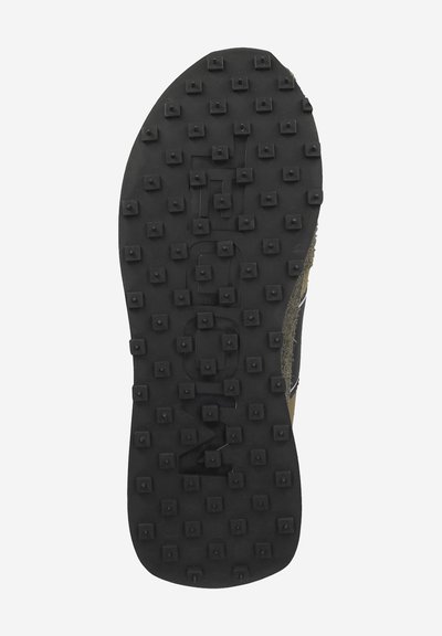 Black rubber shoe sole featuring a patterned grip with square protrusions, textured edges, and a central logo detail.