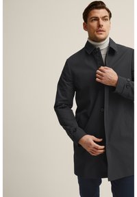 Tummanharmaa vettä hylkivä takki, jossa on muotoiltu kaulus, napitettava etuosa ja sivutaskut. Silkkinen kangastuntuma, tarkasti istuva malli.