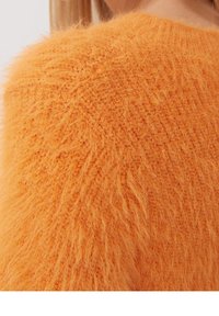 Fluffy oranje trui met een textuurfinish. De stof heeft een zachte, harige uitstraling met een ronde halslijn en ribgebreide afwerking.
