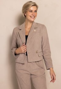 Beiger Cord-Blazer mit kurzem Schnitt, Reverskragen mit Kerbe und Einzelknopfverschluss. Ausgestattet mit strukturiertem Stoff und zwei Vordertaschen.