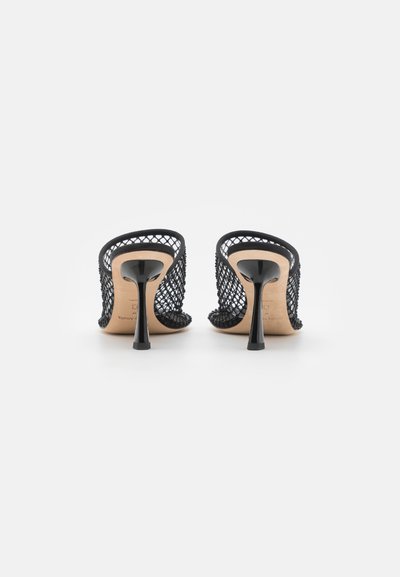 Černé síťované vysoké podpatky s špičatou špičkou a hladkým, lesklým podpatkem. Mají strukturovaný svršek a otevřenou zadní část.