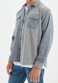 Grijze en blauwe overhemden met verticale strepen, voorzien van twee voorzakken en knoopsluiting. Zachte stoftextuur, casual pasvorm.