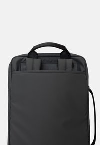 Zaino in tessuto grigio con superficie texturizzata, doppie maniglie superiori e una tracolla laterale regolabile, caratterizzato da un design elegante e minimalista.