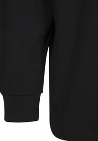 Gros plan du poignet d'une chemise noire à manches longues avec un poignet élastique côtelé et un tissu lisse sur le bras.