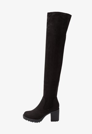 Bottes noires en suède au-dessus du genou avec un talon noir épais. Présentent un bout rond et un panneau élastique sur le côté pour un enfilage facile. Fini texturé.