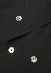 Czarna tkanina o gładkiej fakturze z podwójnym zapięciem na guziki i trzema okrągłymi srebrnymi guzikami, z których każdy ma cztery dziurki.