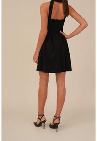 Černé šaty bez rukávů s vypasovaným korzetem a rozšířenou sukní. Obsahují zipové zapínání na zadní straně a sklady kolem pasu. Nosi se s černými vysokými podpatky.