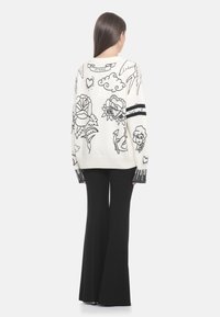 Oversized Pulli in Creme mit schwarzen gestickten Blumen- und Mustermotiven. Mit gerippten Bündchen und einem Logodetail auf der Rückseite.