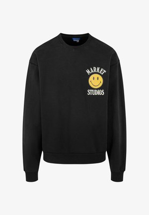Sort sweatshirt med ribbede cuff og kant. Har et trykt gult smiley-ansigt logo og teksten "MARKET STUDIOS" på venstre bryst.