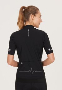 Svart atletisk t-shirt med korta ärmar, figurnära design, andningsbart material, grafisk linje med hjärtslag på baksidan, reflektorerande logotypdetaljer.