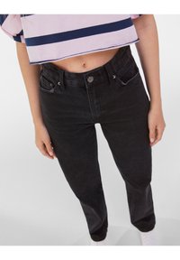 Svarta denimjeans med hög midja, framknappar och fickor. Slät textur, åtstramad passform och subtil blekning vid låren.