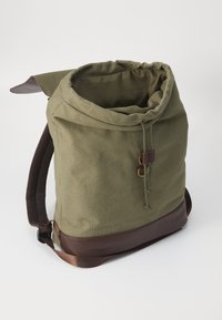 Zaino in tela verde con design a rotolo, base in pelle marrone, chiusura a cordoncino e spallaccio in rete resistente.