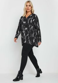 Loose-fitting black and gray patterned blouse with a V-neck and long sleeves, paired with black slim-fit pants and glossy ankle boots.