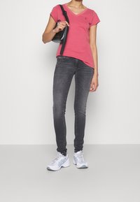 Camiseta de cuello en V rosa de manga corta, combinada con jeans gris ajustados y zapatillas deportivas blancas. Lleva un bolso negro en el hombro.