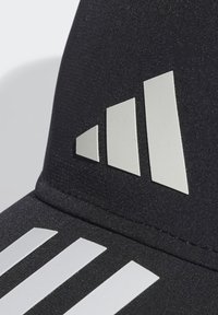 Gorra negra con tres franjas horizontales blancas en la parte frontal y un logotipo reflectante con tres formas diagonales en el lado.