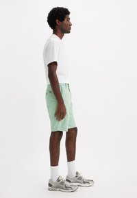 Pantaloni corti verde menta e t-shirt bianca, abbinati a sneaker grigie. I pantaloni corti presentano un design semplice con tasche laterali e senza pattern visibili.