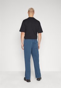Black short-sleeve t-shirt with a crew neck, paired with blue wide-leg pants featuring a side pocket, set against a plain background.