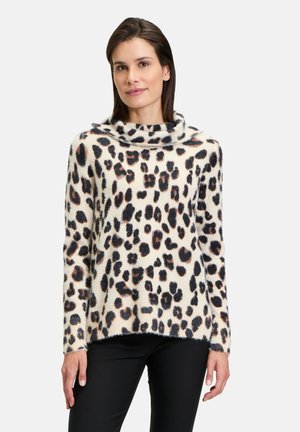 Cremfarbener Pullover mit Schalkragen, der ein schwarz-braunes Leopardenmuster aufweist. Weicher, strukturierter Stoff. Schwarze Hose.