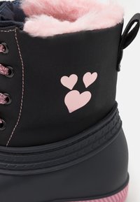 Botte d'hiver noire avec doublure en fausse fourrure rose, motifs en forme de cœur roses et lacets assortis. Dispose d'une semelle extérieure en caoutchouc noir texturée et d'une languette d'aide à l'enfilage.