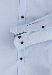 Light blue dress shirt with a smooth texture, black buttons, and contrasting patterned lining in the cuffs. Standard collar and single cuff design.