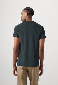 Dunkelgrünes T-Shirt mit kurzen Ärmeln und Rundhalsausschnitt, aus einem weichen Baumwollmix gefertigt, mit lockerer Passform und einfarbiger Struktur.