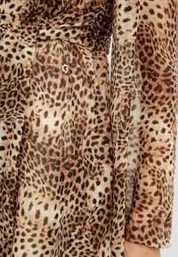 Abito in tessuto trasparente con stampa leopardata, caratterizzato da tonalità di marrone e beige, con un accento metallico "G" e una silhouette fluida.
