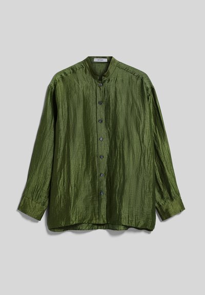 Chemise à manches longues vert olive boutonnée avec un col mandarin et une texture légèrement froissée, posée à plat sur un fond gris.