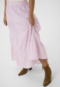 Jupe à volants rayée rose et blanche avec une taille élastique, en tissu fluide et avec un ourlet froncé, assortie à des bottines brunes.