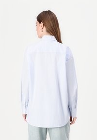 Lyseblå og hvit stripete skjorte med knapper, avslappet passform, lange ermer og detalj med yoke bak, laget av lett stoff.