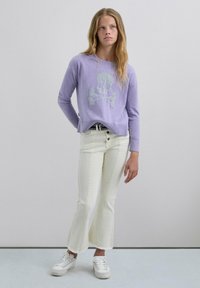 Suéter de punto lavanda con diseño de calavera y huesos cruzados, combinado con jeans acampanados blancos y zapatillas blancas. Tejido ligero, corte relajado.