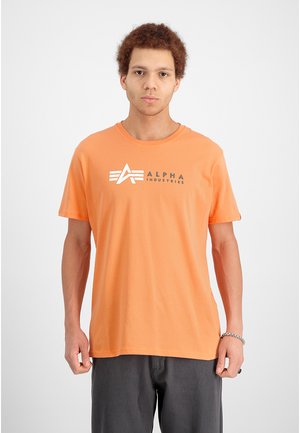 Orange Baumwoll-T-Shirt mit rundem Ausschnitt, kurzen Ärmeln und einem grafischen Logo, das den Markennamen "ALPHA INDUSTRIES" in Grau zeigt.