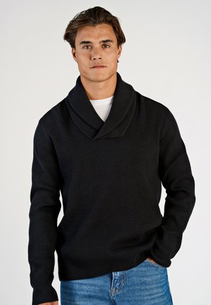 Sort ribbet striktrøje med sjalskrave, der har en afslappet pasform og lange ærmer, parret med lyseblå denim jeans.