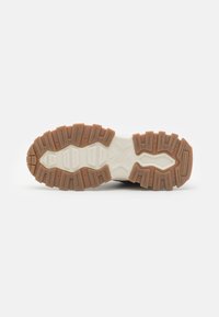 Semelle de chaussure en caoutchouc avec un revêtement à motifs, présentant un design segmenté avec un mélange de matériaux beige et blanc, mettant en avant la durabilité et l'adhérence.