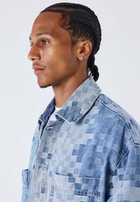 Chaqueta vaquera con un patrón de cuadros en varios tonos de azul, con cuello, dos bolsillos frontales y un acabado texturizado.