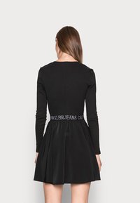Black long-sleeve dress with a fitted bodice and flared skirt, featuring a branded elastic waistband and smooth fabric texture.