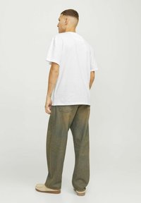 Hvid bomulds t-shirt med korte ærmer, parret med løse olivengrønne jeans. Jeansene har baglommer og en let falmet tekstur.