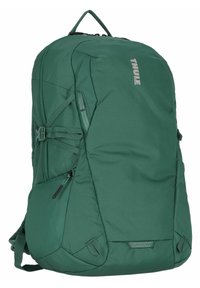 Sac à dos Thule vert avec tissu renforcé, forme ergonomique, bretelles ajustables, fermetures éclair et sangles de compression latérales.