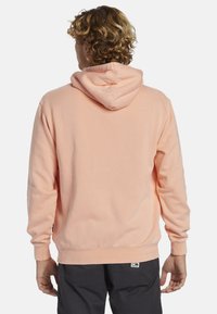 Sudadera con capucha en suave tela de melocotón claro. Presenta puños y dobladillo de canalé, bolsillo tipo canguro y un corte holgado. Marcado mínimo en el dobladillo.