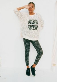 Maglione chiaro con intricati motivi neri, abbinato a leggings scuri con design simili. Scarpe da ginnastica nere completano il look.