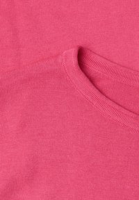 Gros plan sur un tissu tricoté rose vif présentant un col rond plié avec des coutures détaillées et une texture fine.
