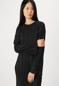 Μαύρο πλισέ φόρεμα με στρογγυλή λαιμόκοψη και μακριά φουσκωτά μανίκια, που διαθέτει κατακόρυφες ραβδώσεις και λεία υφή.