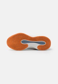 Sokkel med tekstureret orange gummi, der har cirkulære mønstre; hvid mellemsål og lyseblå accenter integreret i designet.