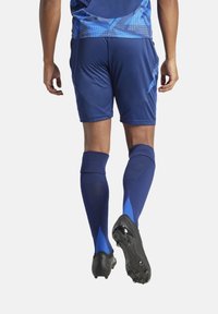 Blauwe sporttrui met geometrische patronen, bijpassende blauwe shorts en blauwe sokken, aangevuld met zwarte voetbalschoenen.