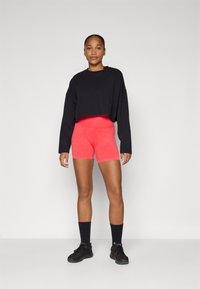 Black cropped long-sleeve top paired with high-waisted, bright red shorts. Model wears black sneakers and crew-length black socks.