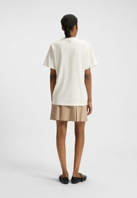 Creme kortærmet top med en afslappet pasform, syninger på bagsiden, kombineret med en plisseret beige nederdel og sorte flade sko.