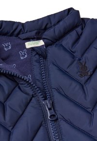 Námořnická prošívaná péřovka s vysokým límcem a předním zipem. Vnitřní podšívka má modrý motiv králíčka a logovou nášivku.