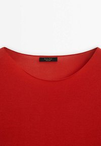 Haut en maille rouge avec un col rond et une étiquette noire cousue à l'intérieur du col.