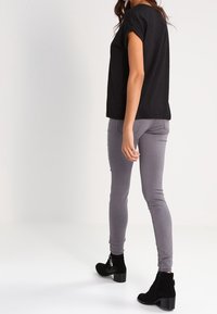 Camisa negra de manga corta, jeans gris claro de corte slim y botas negras hasta el tobillo con un diseño texturizado. Enfoque en formas simples y modernas, y colores neutros.