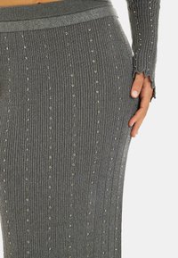 Tejido de punto ribeteado gris con pequeñas lentejuelas. Presenta un diseño ajustado y una pretina texturizada, con un borde con forma de ondas en las mangas.