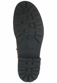 Semelle en caoutchouc noir avec un motif de texture présentant des motifs en forme d'étoile et des rainures, marqué "Clarks". Le bord est arrondi et lisse.